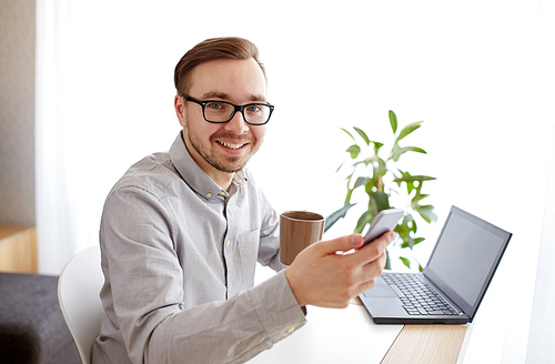 business, startup, technology and people concept - happy businessman or creative male worker texting on smarphone and drinking coffee at home office