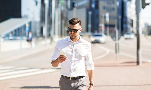 business, technology, communication and people concept - young man in sunglasses with smartphone walking in city