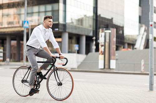 lifestyle, transport and people concept - young man with headphones riding bicycle on city street