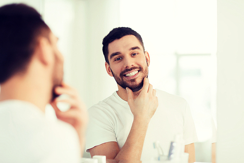 beauty, hygiene and people concept - smiling young man looking to mirror at home bathroom