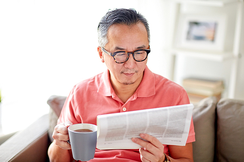 leisure, information, people and mass media concept - happy man in glasses reading newspaper and drinking tea at home