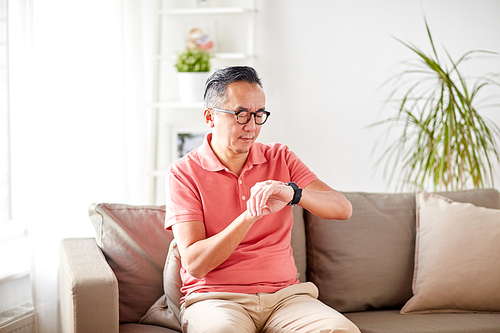 people, punctuality and time concept - asian man looking at his wristwatch at home