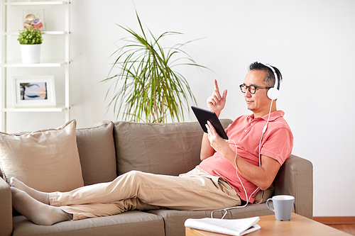 technology, people and lifestyle concept - happy man with tablet pc computer and headphones listening to music at home