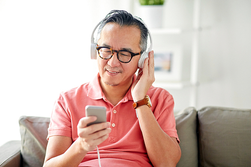 technology, people and lifestyle concept - happy man with smartphone and headphones listening to music at home