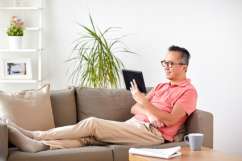 technology, people and lifestyle concept - man with tablet pc sitting on sofa at home