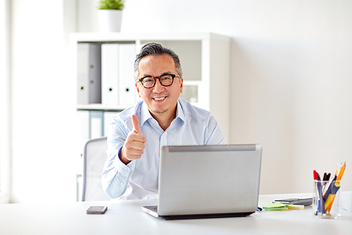 business, people and technology concept - happy smiling businessman in eyeglasses with laptop computer showing thumbs up at office