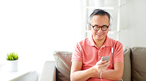 technology, people and lifestyle concept - happy man with smartphone and headphones listening to music at home