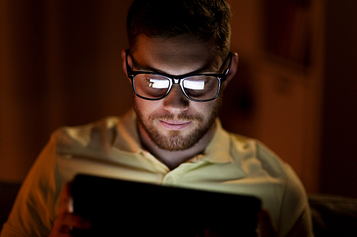 technology, internet, communication and people concept - young man in glasses with tablet pc computer networking at night at home