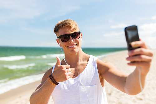 summer holidays and people concept - happy smiling young man with smartphone taking selfie on beach