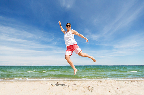 summer holidays and people concept - happy smiling young man jumping on beach