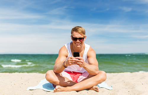 summer holidays and people concept - happy smiling young man with smartphone sunbathing on beach towel