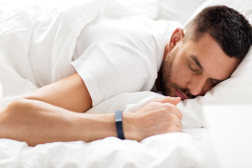 people, bedtime and rest concept - man with smartwatch sleeping in bed