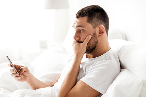 technology, internet, communication and people concept - young man texting on smartphone in bed at home in morning