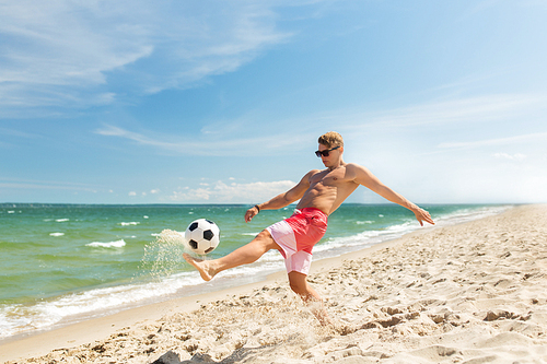 football, sport, fitness and people concept - young man with ball playing soccer on summer beach