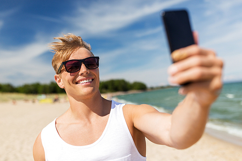 summer holidays and people concept - happy smiling young man with smartphone taking selfie on beach
