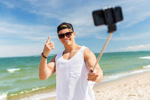 summer holidays and people concept - happy smiling young man with smartphone selfie stick taking picture on beach