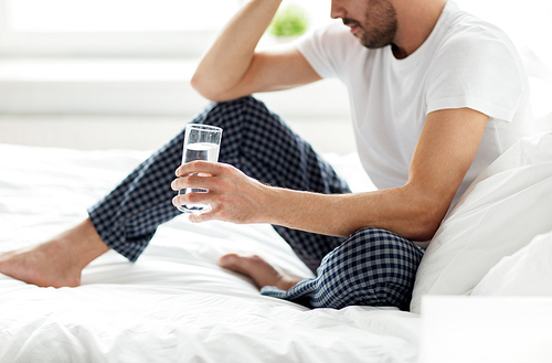 people, bedtime and rest concept - man in bed with glass of water at home