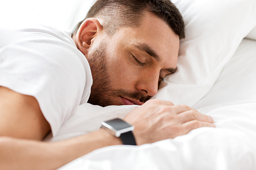 people, bedtime and rest concept - close up of man with smartwatch sleeping in bed