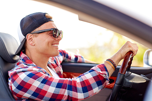 summer holidays, travel, road trip and people concept - happy smiling young man in sunglasses and cap driving convertible car