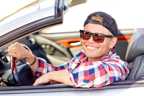 summer holidays, travel, road trip and people concept - happy smiling young man in sunglasses and cap driving convertible car