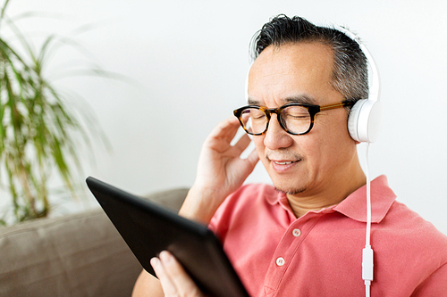 technology, people and lifestyle concept - happy man with tablet pc computer and headphones listening to music at home