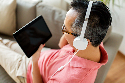 technology, people and lifestyle concept - close up of man with tablet pc computer and headphones listening to music at home