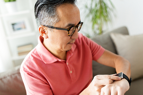 people, modern technology and time concept - close up of asian man with smart watch at home