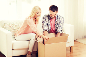 people, delivery, shipping and postal service concept - happy couple opening cardboard box or parcel at home
