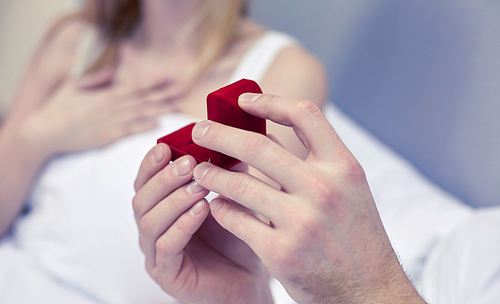 proposal, people, love, holidays and happiness concept - close up of hands holding little red gift box with engagement ring