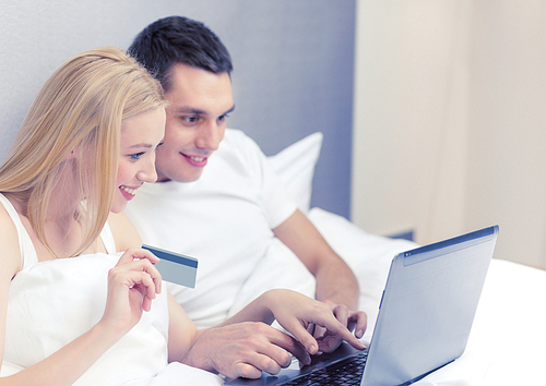 hotel, travel, relationships, technology, internet and happiness concept - smiling couple in bed with laptop and credit card