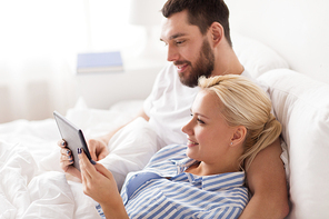 family, technology, internet and people concept - smiling happy couple with tablet pc computer in bed at home bedroom