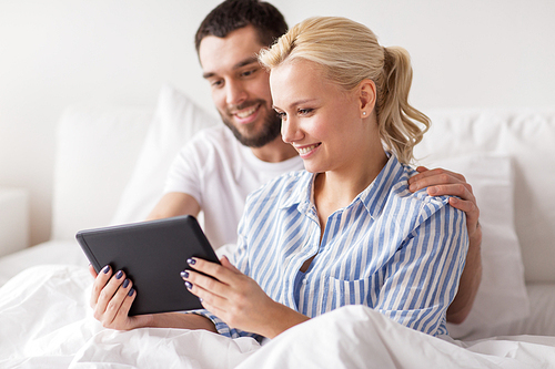 family, technology, internet and people concept - smiling happy couple with tablet pc computer in bed at home bedroom