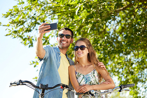 people, technology and lifestyle concept - happy couple with bicycles taking selfie by smartphone at country in summer