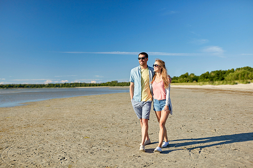 leisure, relationship and people concept - happy couple in sunglasses walking along summer beach