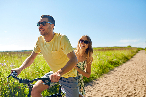 people, leisure and lifestyle concept - happy young couple riding bicycle together in summer