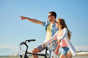 people, leisure and lifestyle concept - happy young couple riding bicycles at seaside