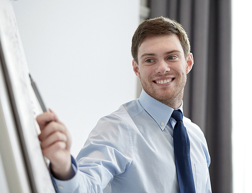 business and people concept - smiling businessman pointing marker to flipboard on presentation in office