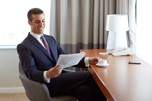 business, people and mass media concept - happy smiling businessman reading newspaper and drinking coffee at hotel room