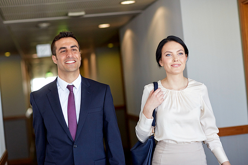 business trip and people concept - man and woman with bag at office or hotel corridor