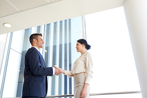 business, partnership and people concept - smiling man and woman shaking hands at office