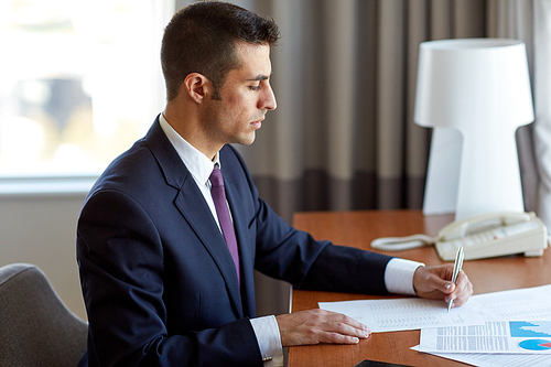 business, people and paperwork concept - businessman with papers working at hotel room