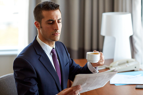 business, people and mass media concept - businessman reading newspaper and drinking coffee at hotel room