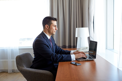 business trip, people and technology concept - businessman typing on laptop at hotel room
