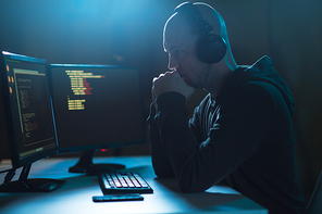 cybercrime, hacking and technology concept - male hacker with headphones and coding on laptop computer screen wiretapping or using computer virus program for cyber attack in dark room