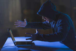 cybercrime, hacking and technology crime - angry male hacker with laptop computer in dark room
