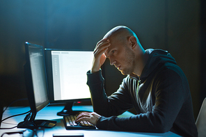 cybercrime, hacking and technology concept - male hacker in dark room having problem with computer virus program for cyber attack