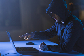 cybercrime, hacking and technology crime - male hacker pointing finger at laptop computer in dark room