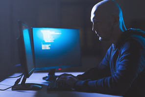 cybercrime, hacking and technology concept - male hacker in dark room writing code or using computer virus program for cyber attack