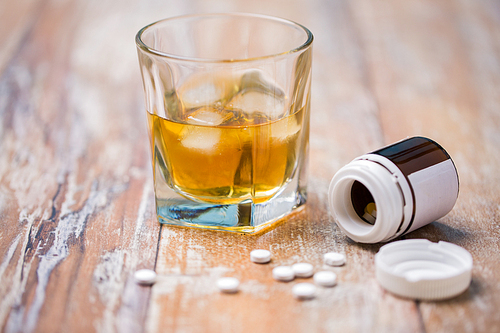 drug abuse, addiction and suicide concept - glass of alcohol and pills on table