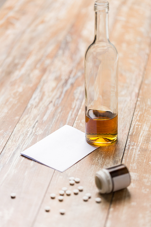 drug abuse, addiction and suicide concept - bottle of alcohol and pills on table